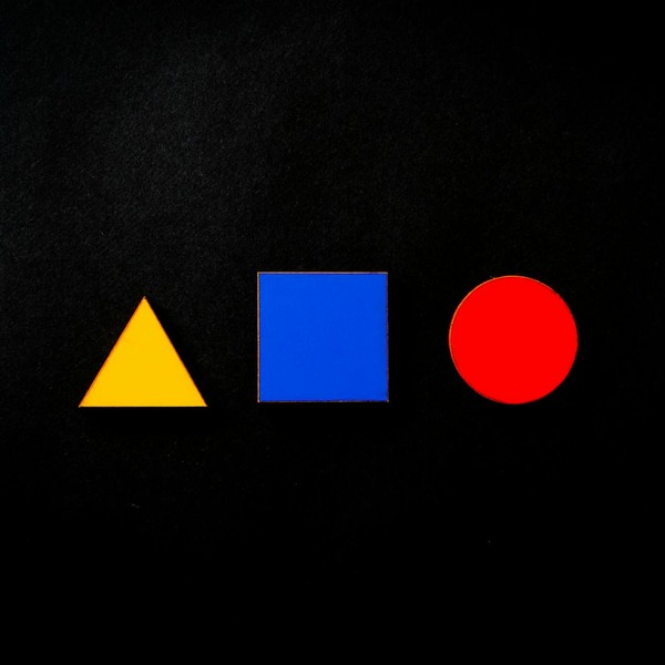 Vivid geometric shapes of triangle, square, and circle in primary colors on a black background.